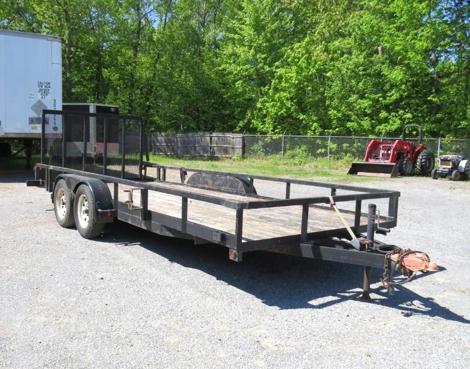 Black utility trailer on gravel, with black metal side rails and a mesh gate.