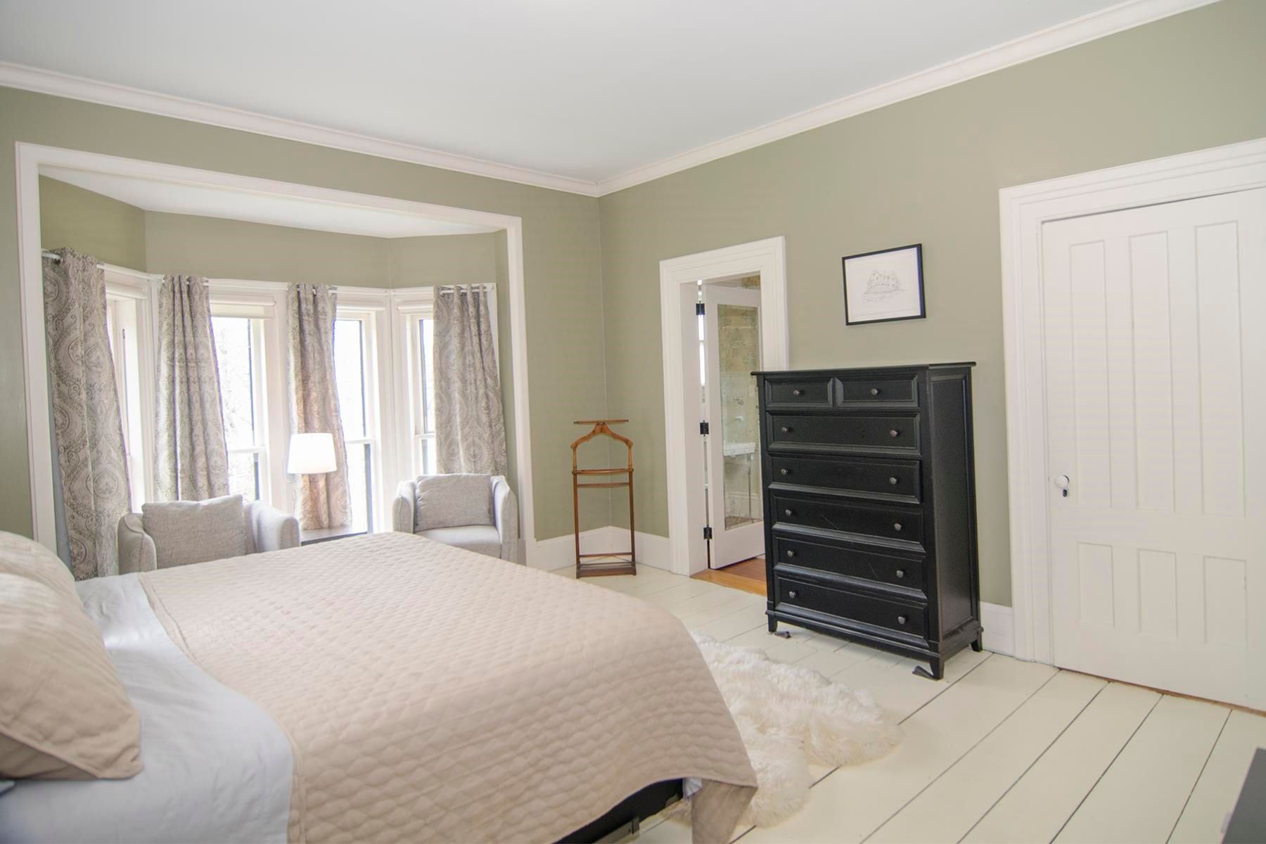 Bedroom with bed, bay window with curtains, black dresser, light green walls.