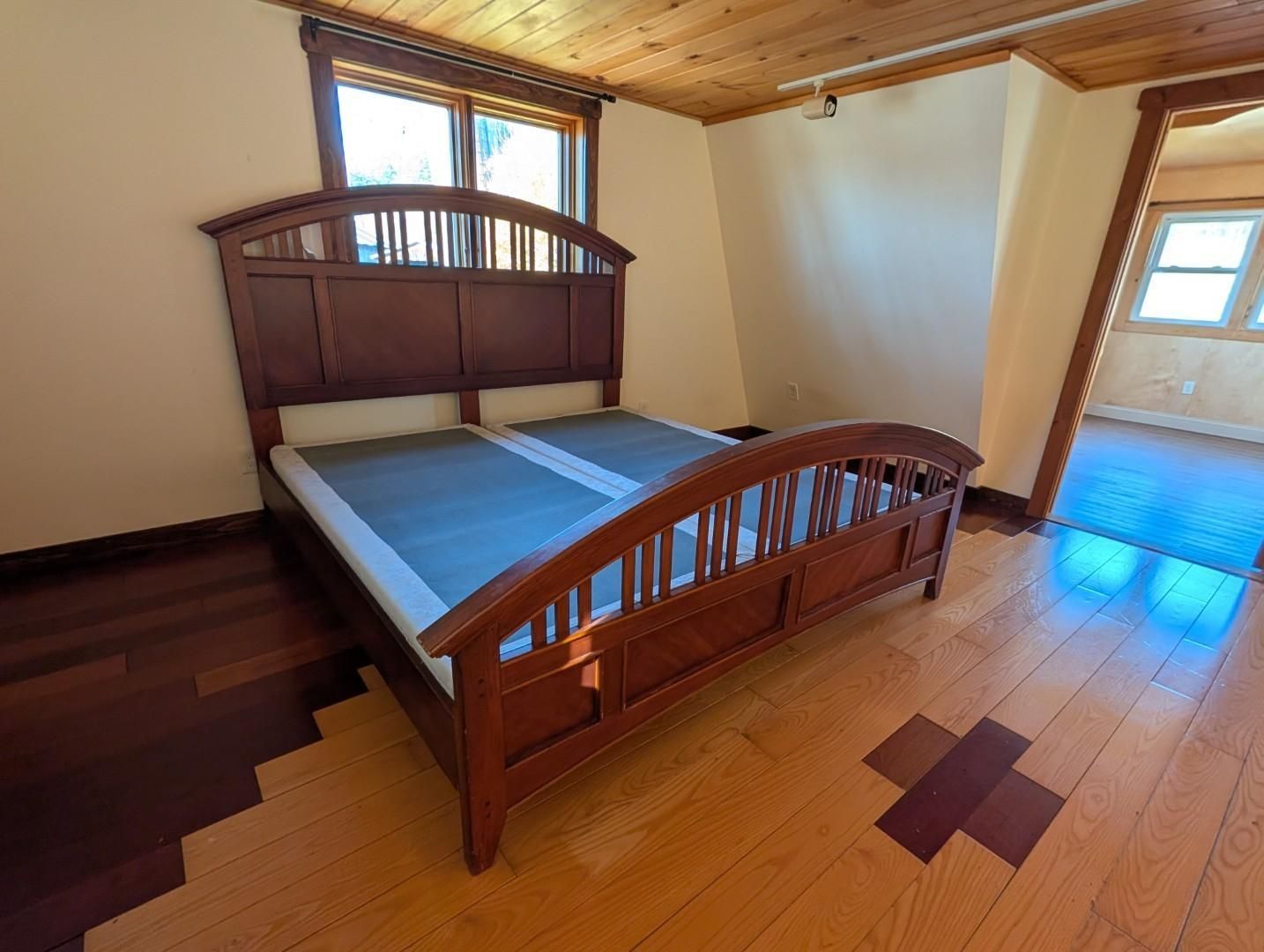 Wooden bed with blue bedding in a sunlit empty bedroom with hardwood floors