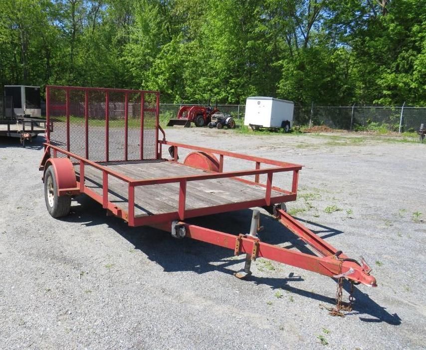 Red utility trailer with a mesh gate, parked outside on a paved lot.