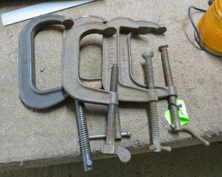C-clamps of various sizes and conditions rest on a light-colored surface, possibly a workbench.