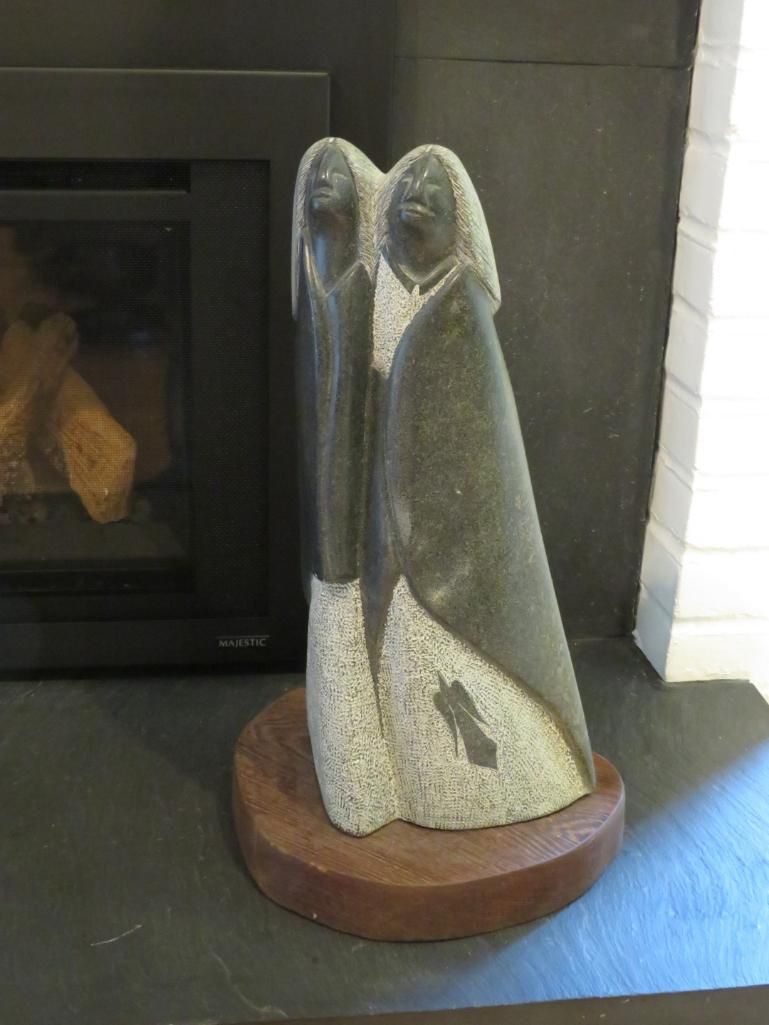 Stone sculpture of two figures on a wooden base.