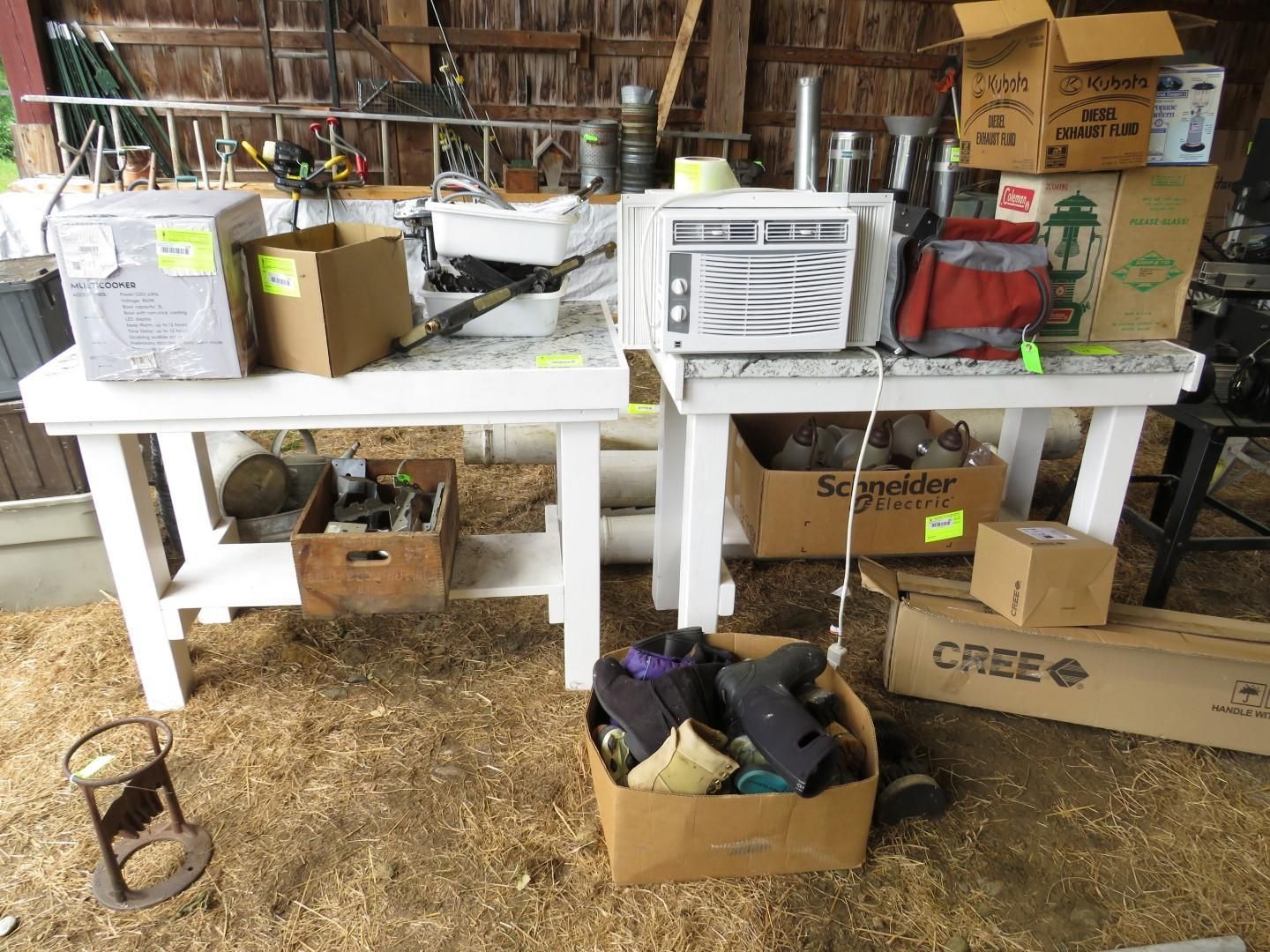 Two white tables with items in a barn. Boxes, an AC unit, tools, and a lantern are visible.
