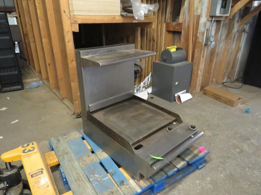 Stainless steel commercial flat-top grill on a blue pallet in a workshop.