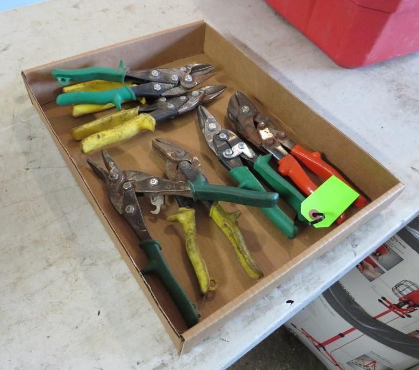 A cardboard box filled with various metal snips with colorful handles.