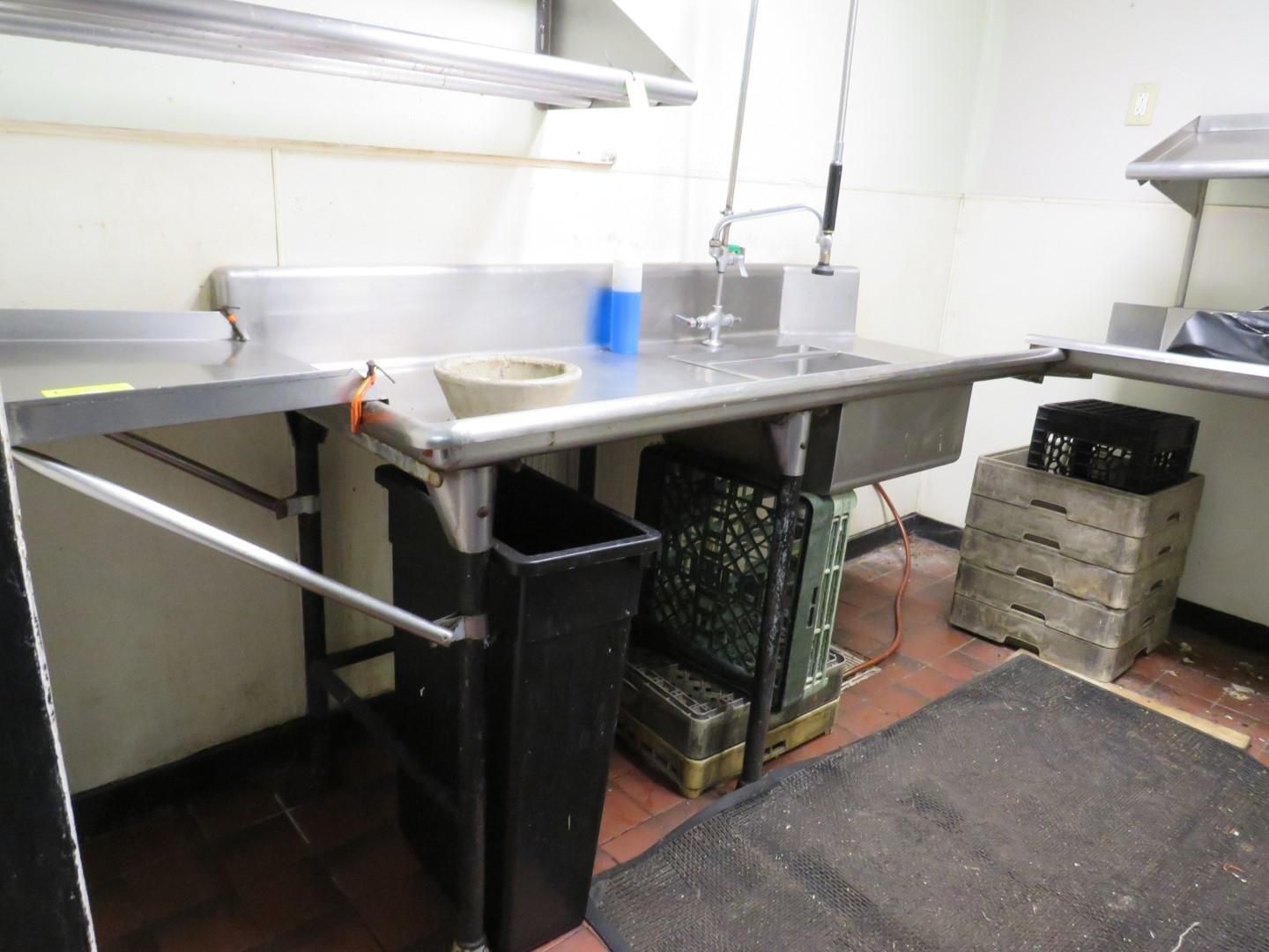 Stainless steel kitchen sink with trash bin, a black mat, and boxes on the floor.