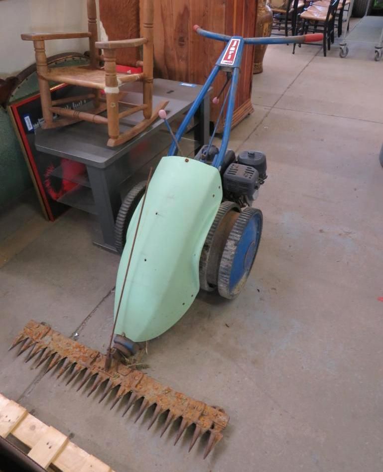 Light green and blue sickle bar mower on a concrete floor.