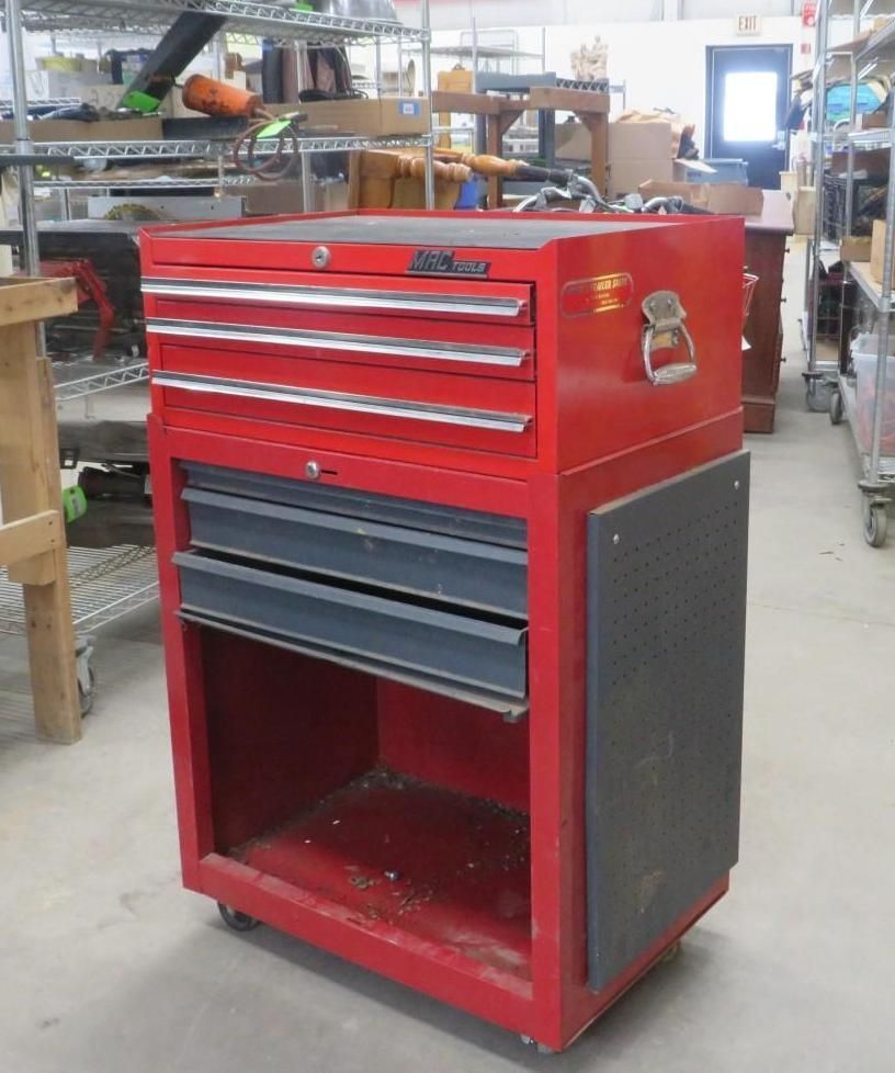 Red tool chest with drawers and open shelf on wheels in a workshop.