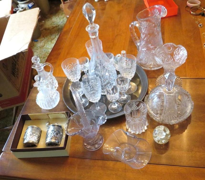 Assortment of crystal glassware on a wooden table, including decanters, pitchers, glasses, and a silver tray.