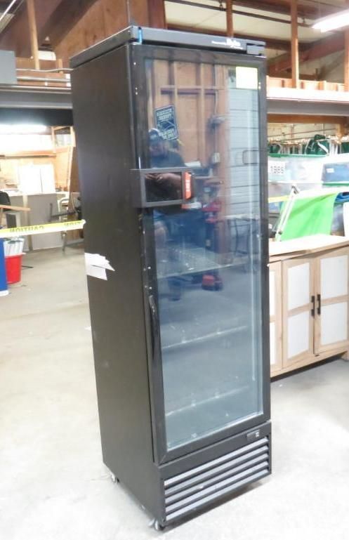 Tall, black commercial refrigerator with glass door in a workshop.