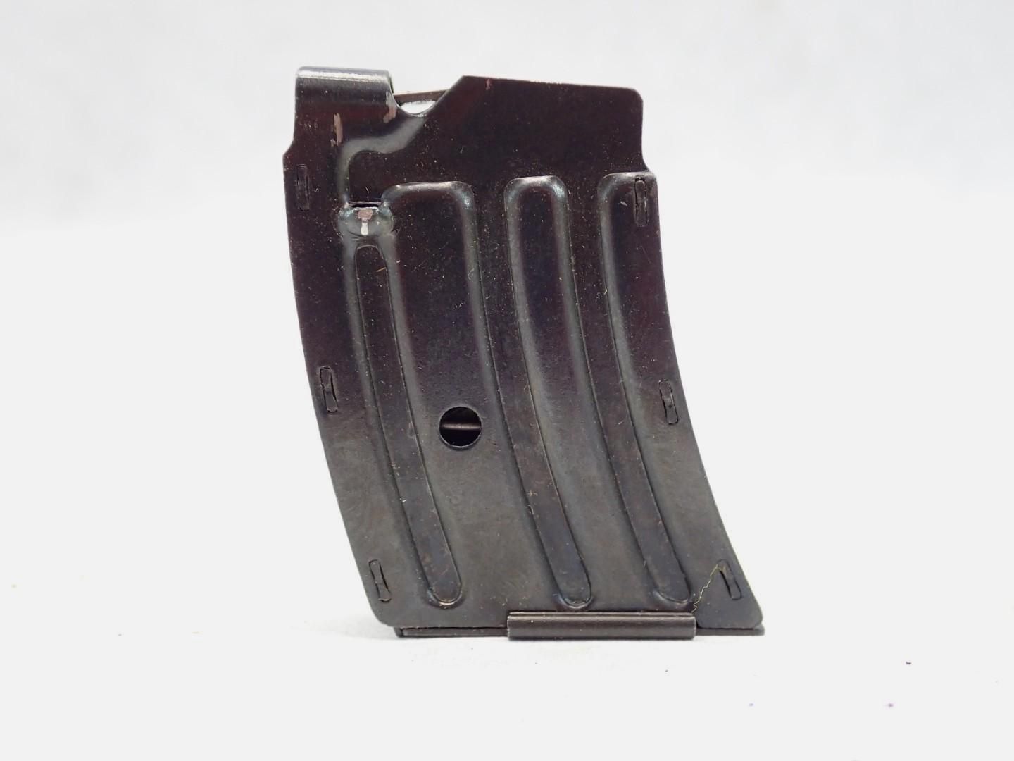 A dark metal firearm magazine, curved with a follower pin.