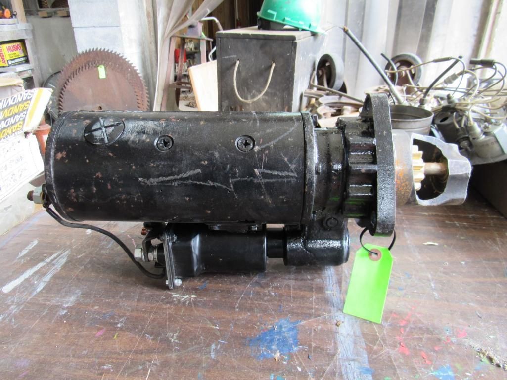 Black starter motor on a wooden surface, with a green tag. Workshop background.