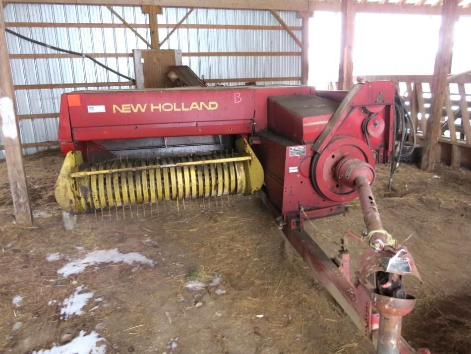 Red and yellow New Holland hay baler inside a barn.