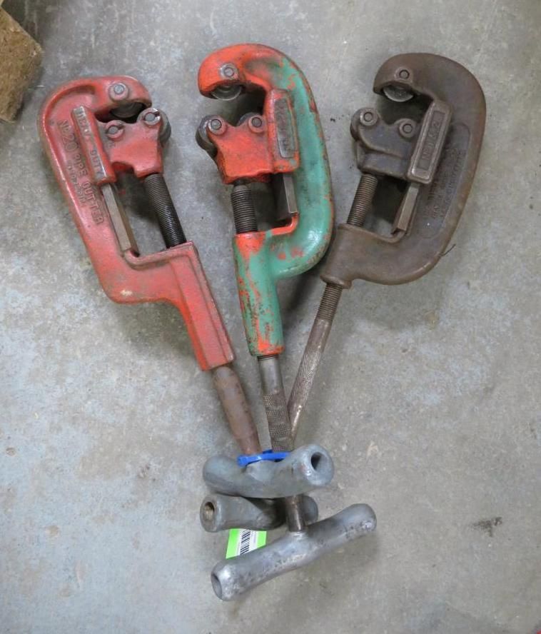 Three pipe cutters with red, green, and gray handles on a concrete surface.