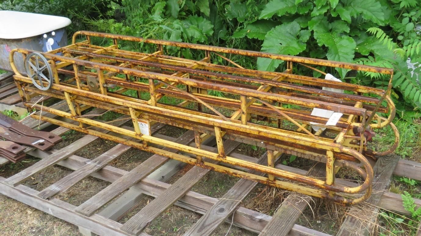Yellow metal frame, farm equipment, on wooden pallets outdoors.