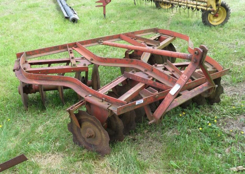 Red disc harrow on grassy ground.