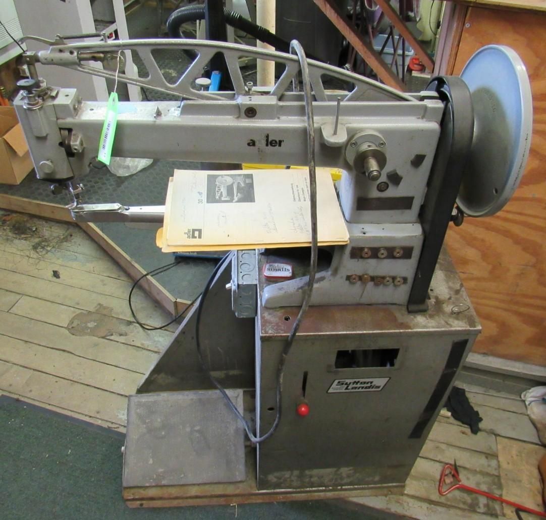 Industrial sewing machine, metallic gray, mounted on a cabinet with a foot pedal.