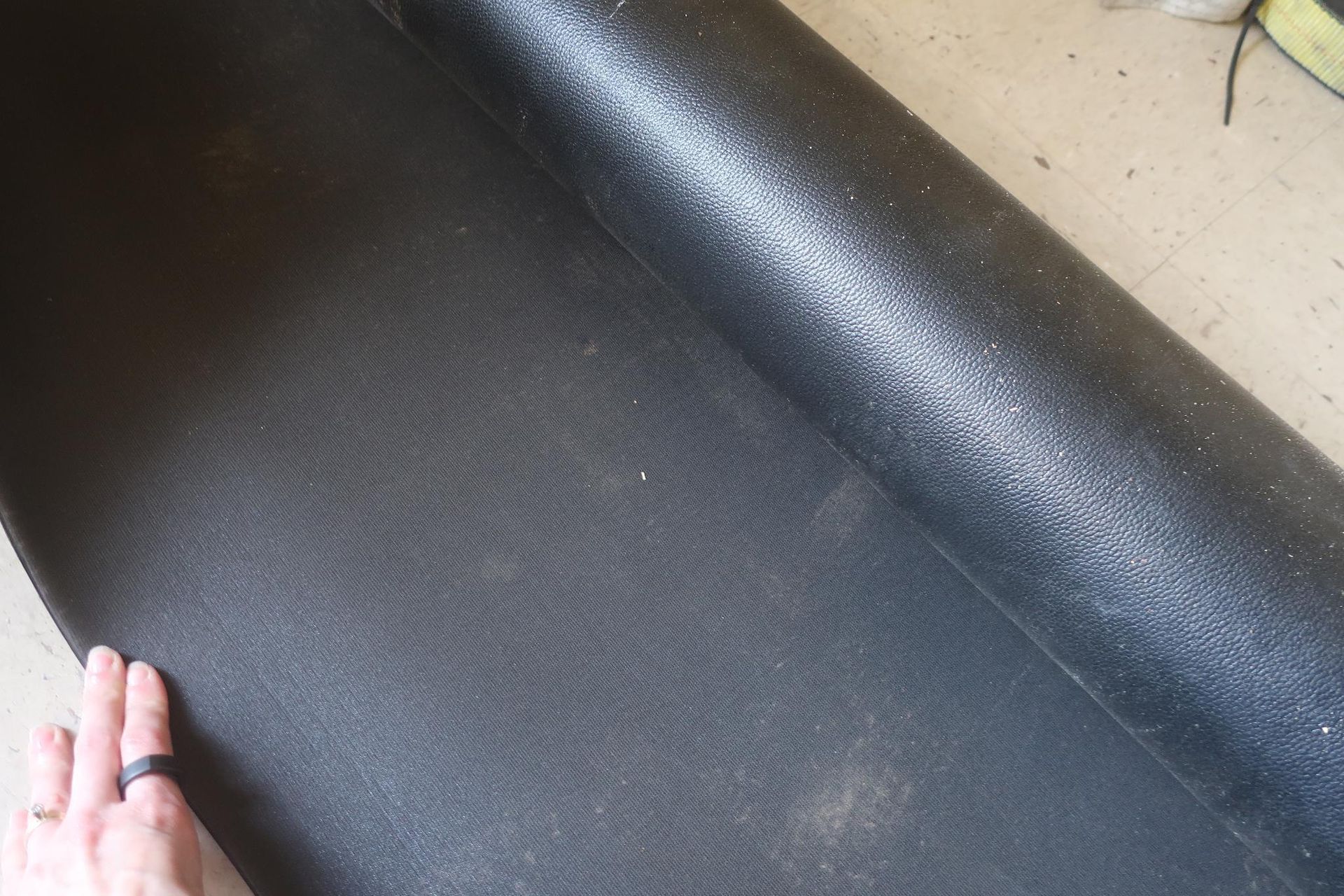 Hand touching a rolled-up, black, textured rubber mat on a concrete floor.