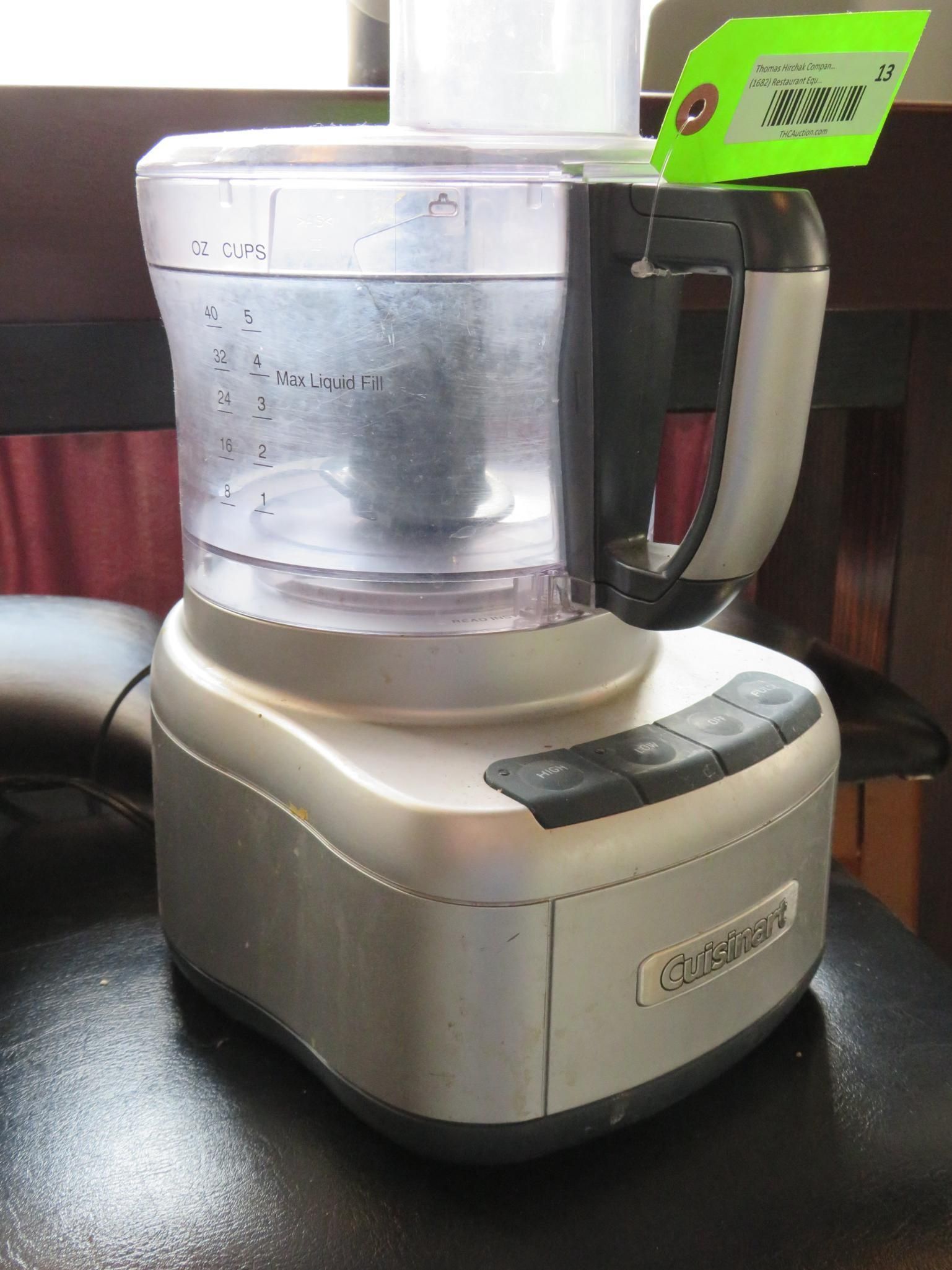 Silver food processor with a clear plastic bowl, handle, and a green tag attached.