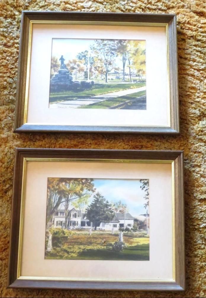 Two framed landscape paintings of buildings and trees, in fall colors.