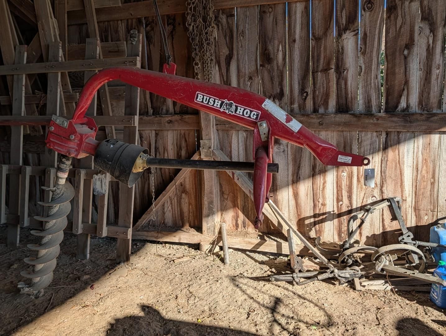 Red excavator auger attachment inside a rustic wooden shed