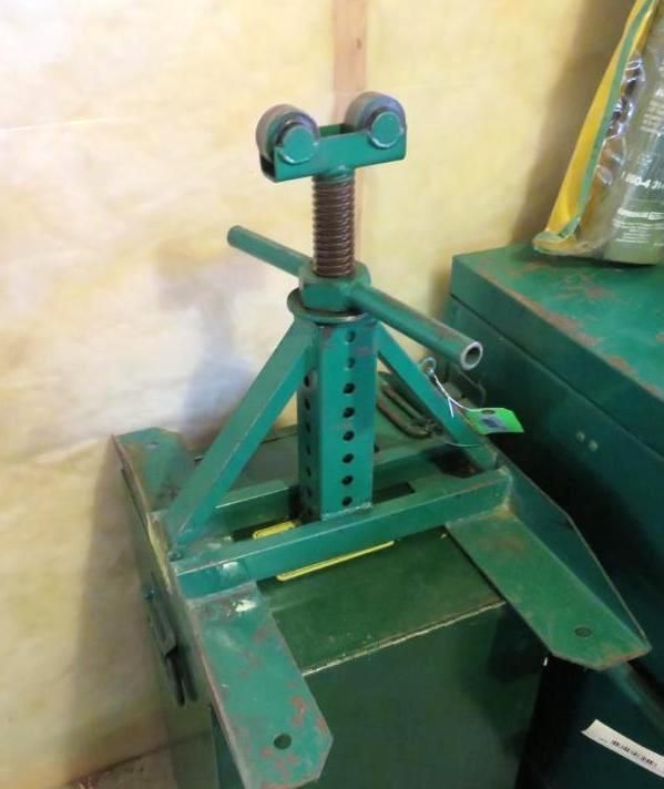 Green pipe stand with adjustable rollers, on a green metal box.