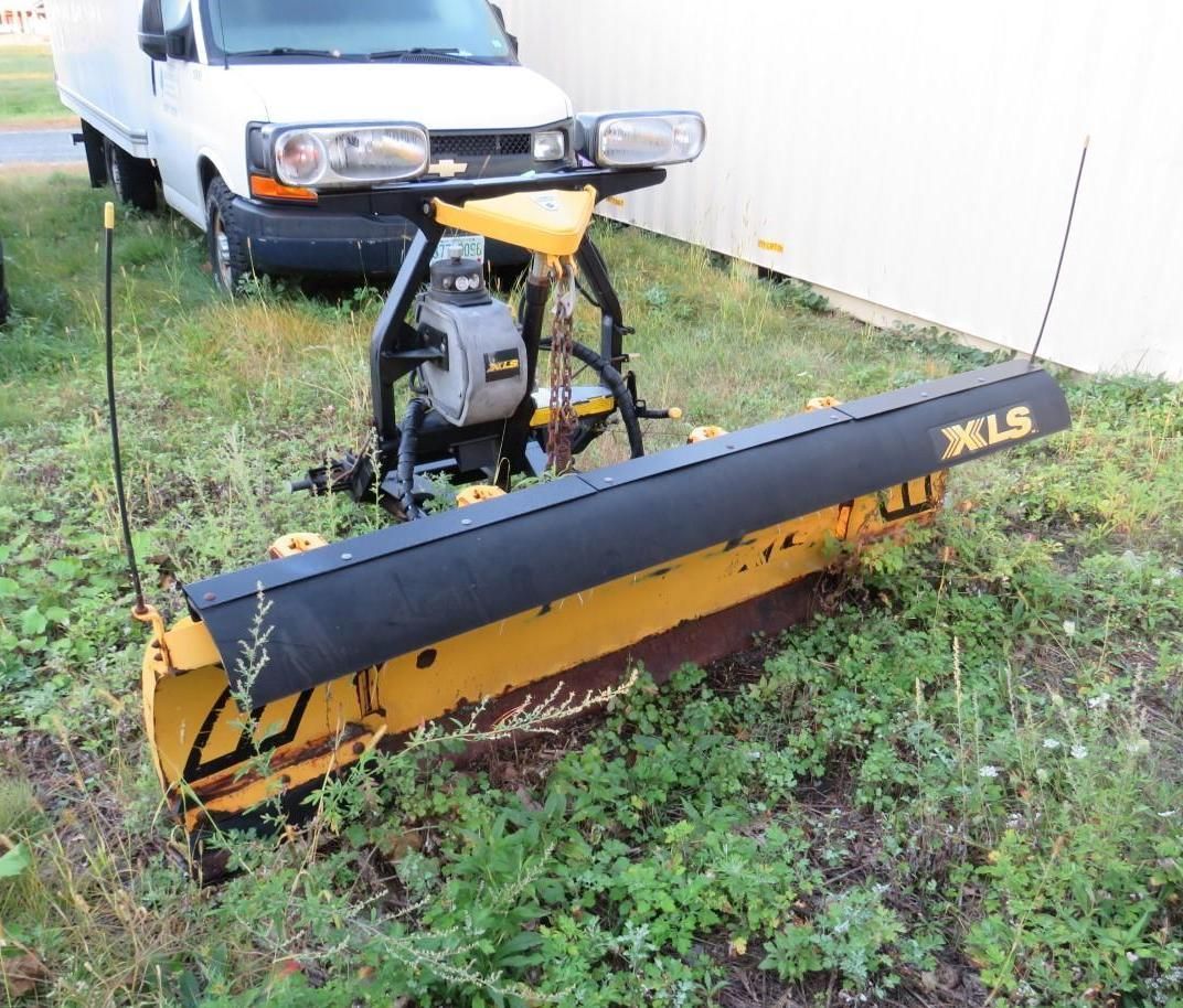 Yellow snowplow in front of a white truck, on grass.