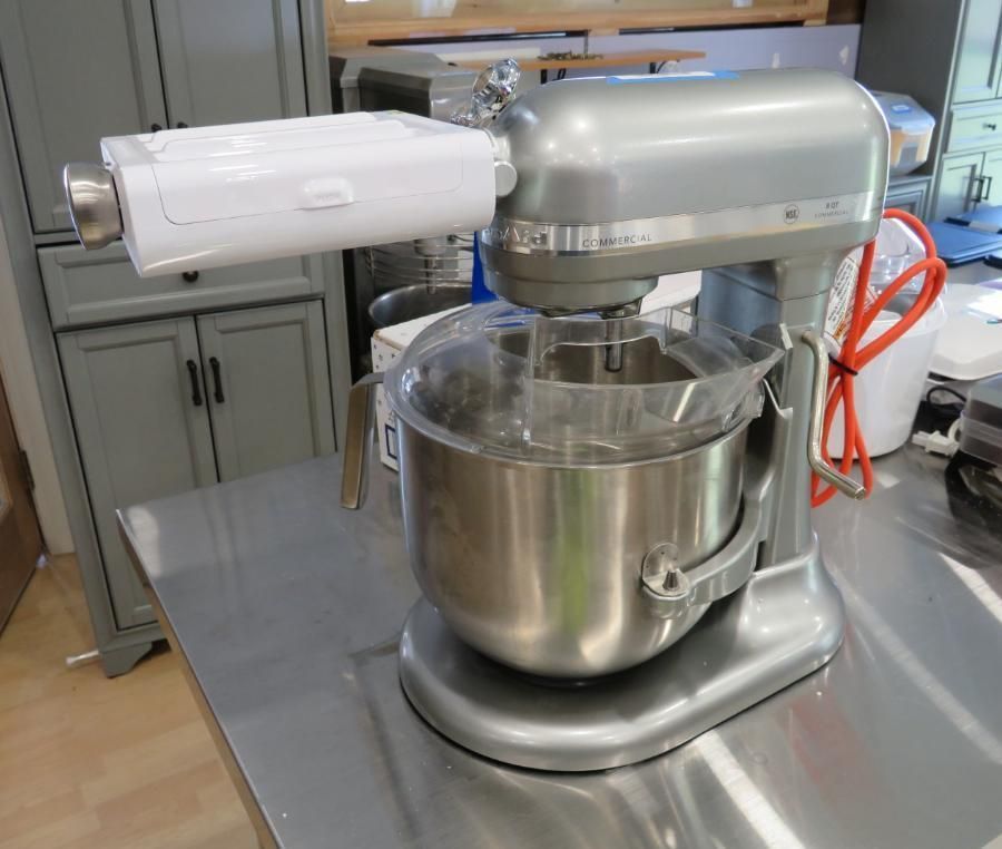 Silver KitchenAid mixer with attached food grinder on a stainless steel counter.