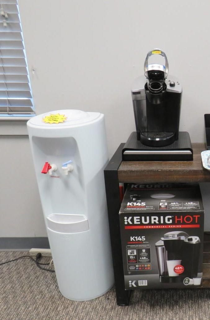 White water cooler and a Keurig coffee maker on a shelf next to a window.