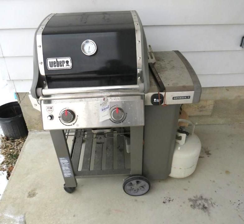 Weber Spirit II gas grill on a concrete patio, with a propane tank and black lid.