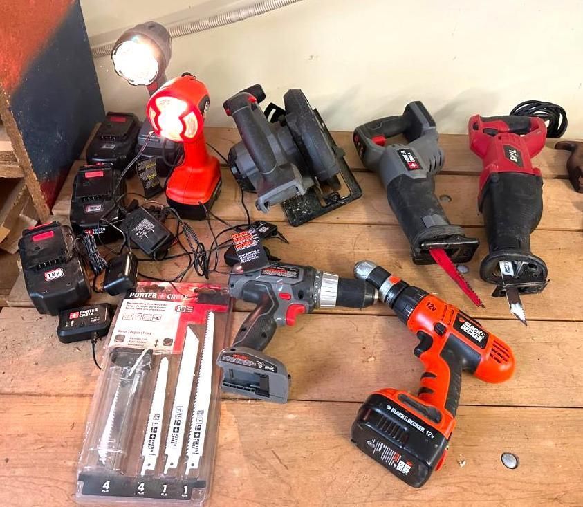 A collection of cordless power tools in red and black on a wooden surface, including a circular saw and drill.