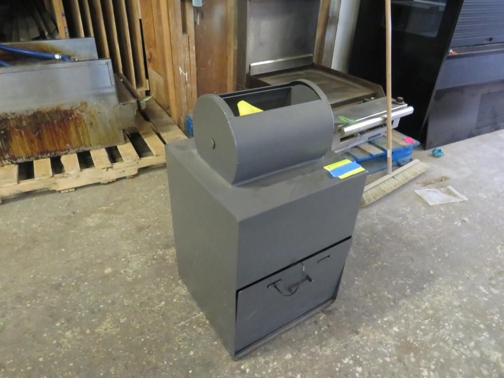 Gray metal trash can with a cylindrical top and drawer in a workshop.