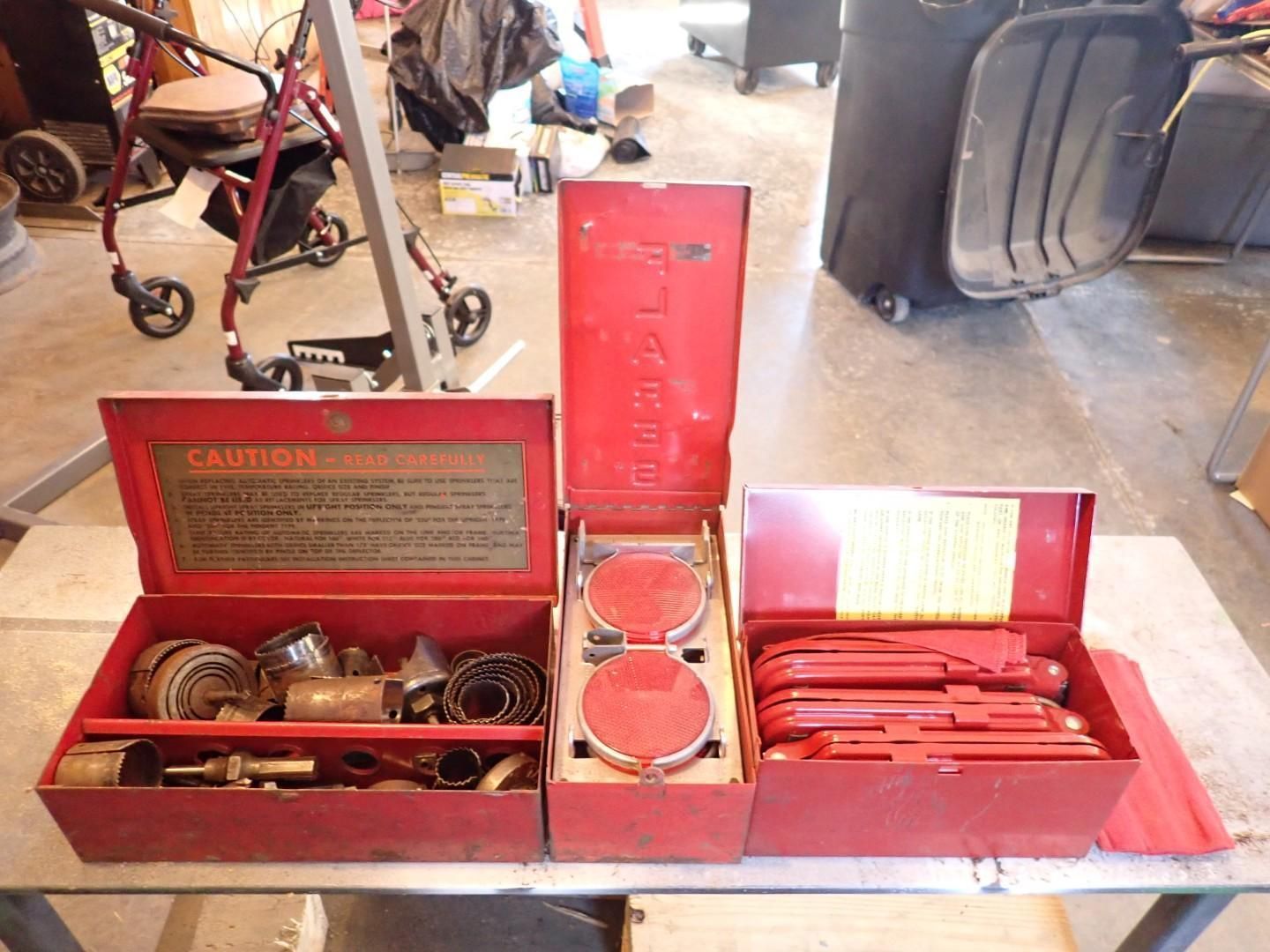 Open red toolbox filled with assorted coins, medals, and small metal items on a garage floor