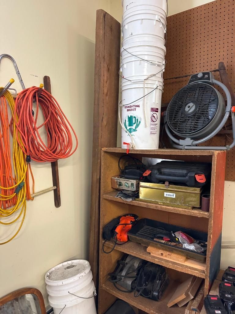 Workshop tools and supplies on shelves and hanging on a wall; extension cords, buckets, fan.