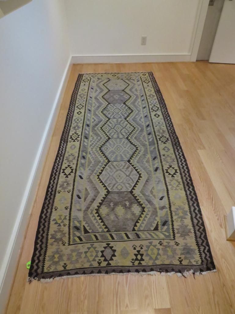 Rug with geometric patterns on a wooden floor, next to a white wall.
