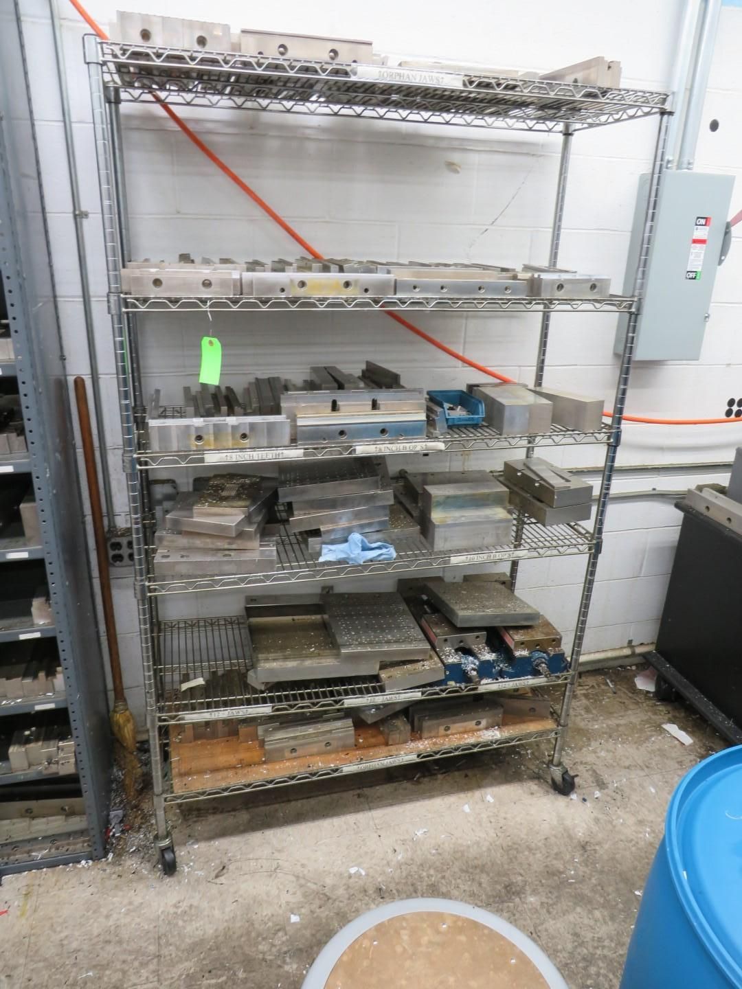 Metal shelving unit filled with industrial metal blocks and parts in a workshop setting.