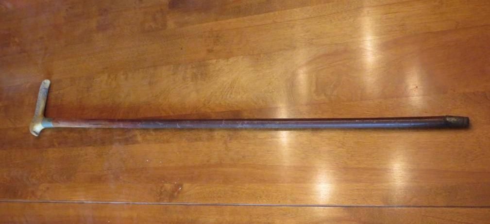 Wooden walking stick with a curved metal handle rests on a wood surface.