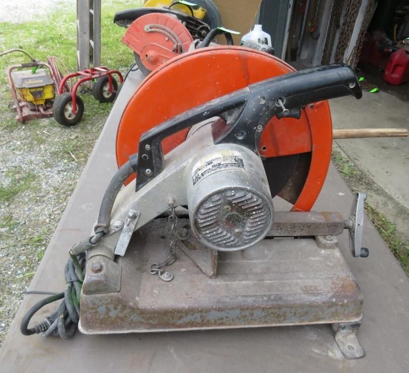 Metal-cutting saw with an orange blade guard and a black handle, resting on a metal surface outdoors.