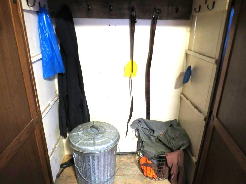 Small storage space with hooks, a trash can, clothing, and belts.