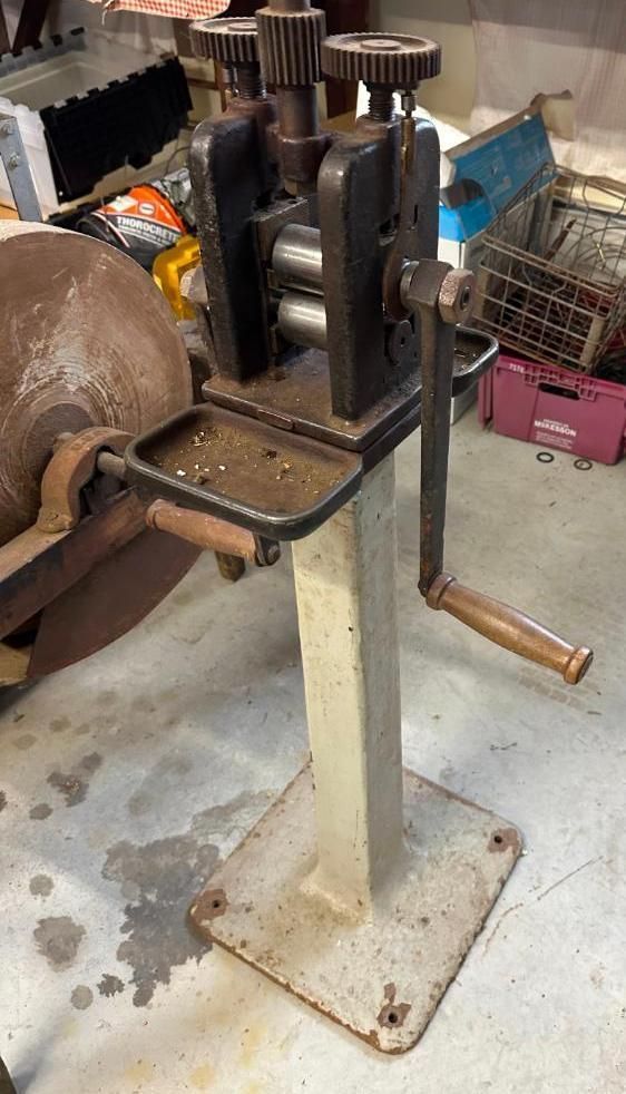 Metal rolling mill with hand crank, mounted on a stand.