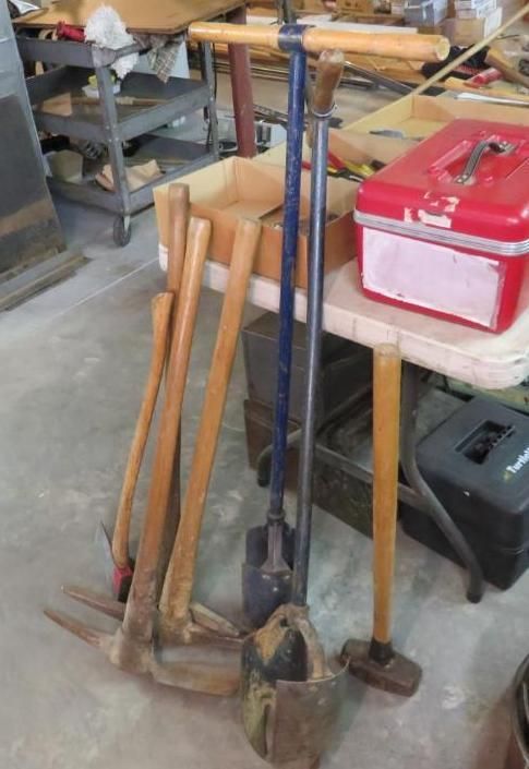 Tools with wooden handles: picks, post hole digger, and sledgehammer.