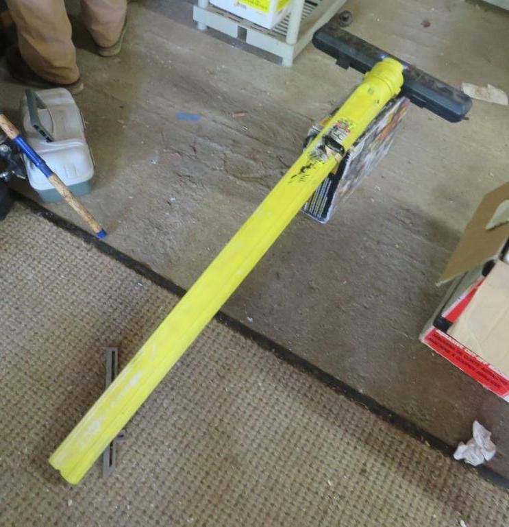 Yellow pole tool with black handle, resting on a carpet.
