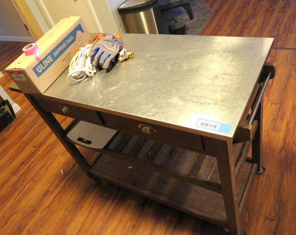 Wooden kitchen cart with stainless steel top, and supplies on top.