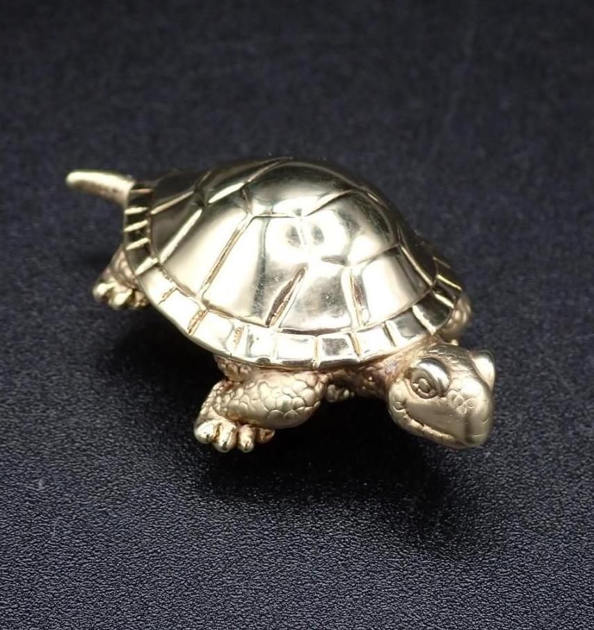 Gold-colored turtle figurine on a black surface.