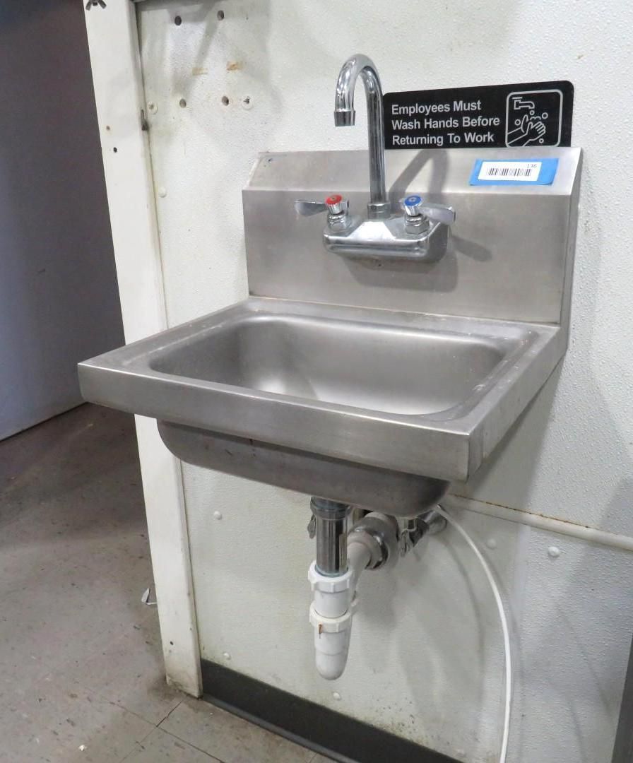 Stainless steel sink mounted on a wall with a faucet and drain.
