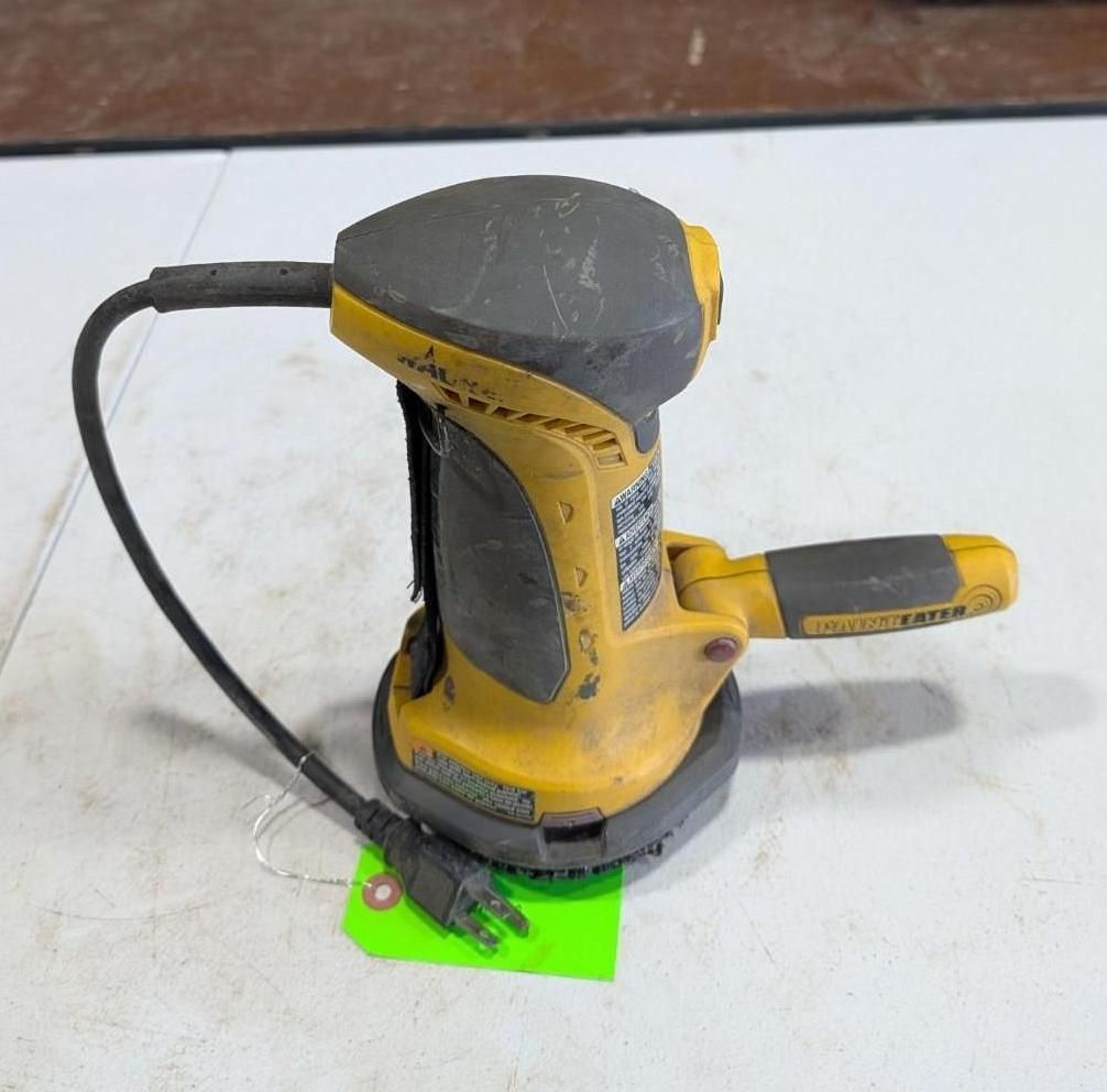 Yellow and black electric handheld sander with cord on a white surface, resting on a small green tag
