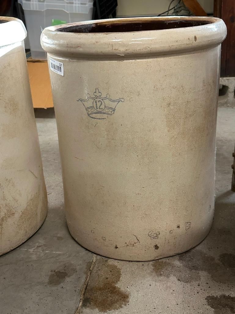 Tan stoneware crock with a faded blue emblem, on a concrete surface.