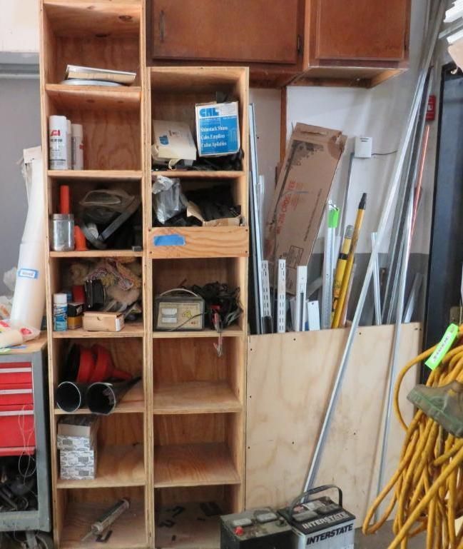 Wooden shelves holding various tools and supplies in a garage, next to a vertical storage area for long items.
