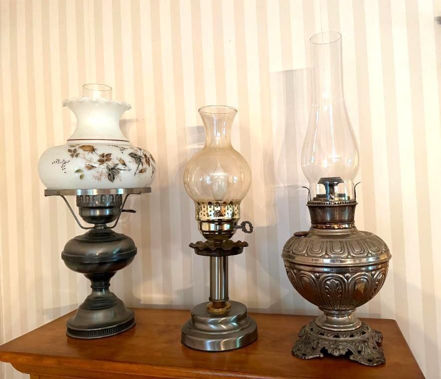 Three antique oil lamps on a wooden surface, set against a striped wall.