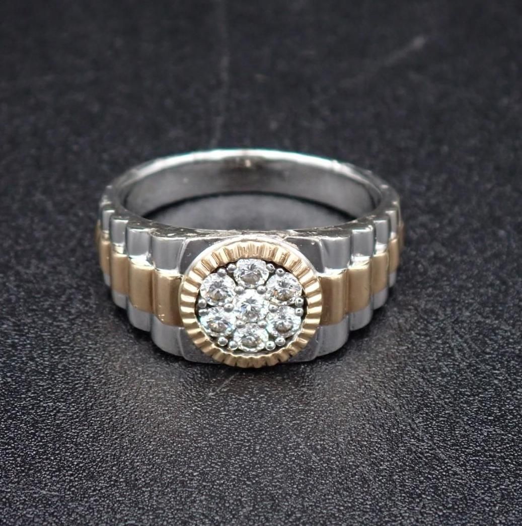 Diamond ring with a two-tone band, gold-tone center with six diamonds, set against a dark textured surface.